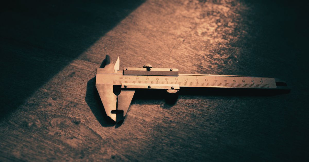 A single precision measuring calliper resting on a dark workbench, strong directional light casting a long defined shadow