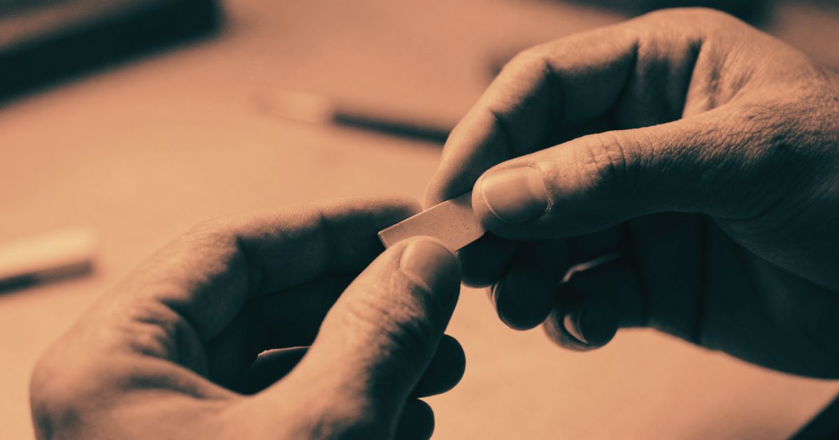 Close-up of a craftsperson's hands holding a small finished component, strong raking light highlighting surface texture