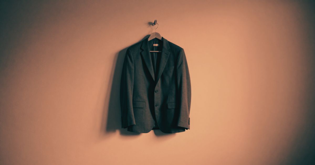 A single business suit jacket hanging on a wooden peg in an empty room