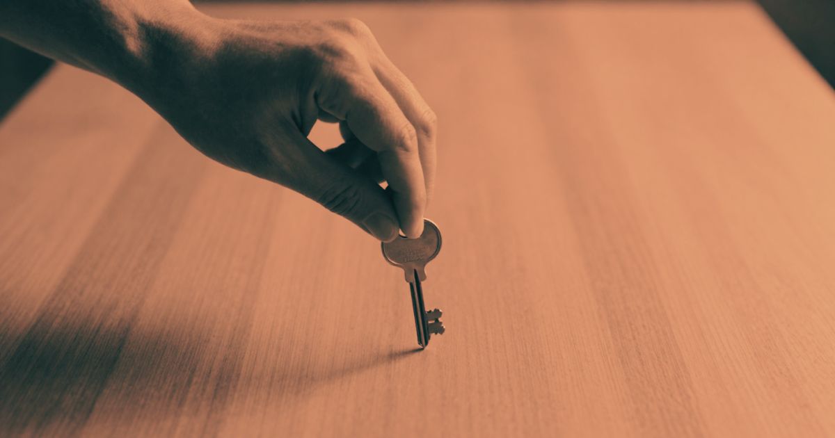 A hand setting a single key down on a bare wooden table, shot from above