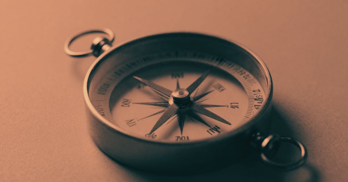 A blurred compass resting on an unmarked surface, the needle visible but the markings unreadable, heavy shadow
