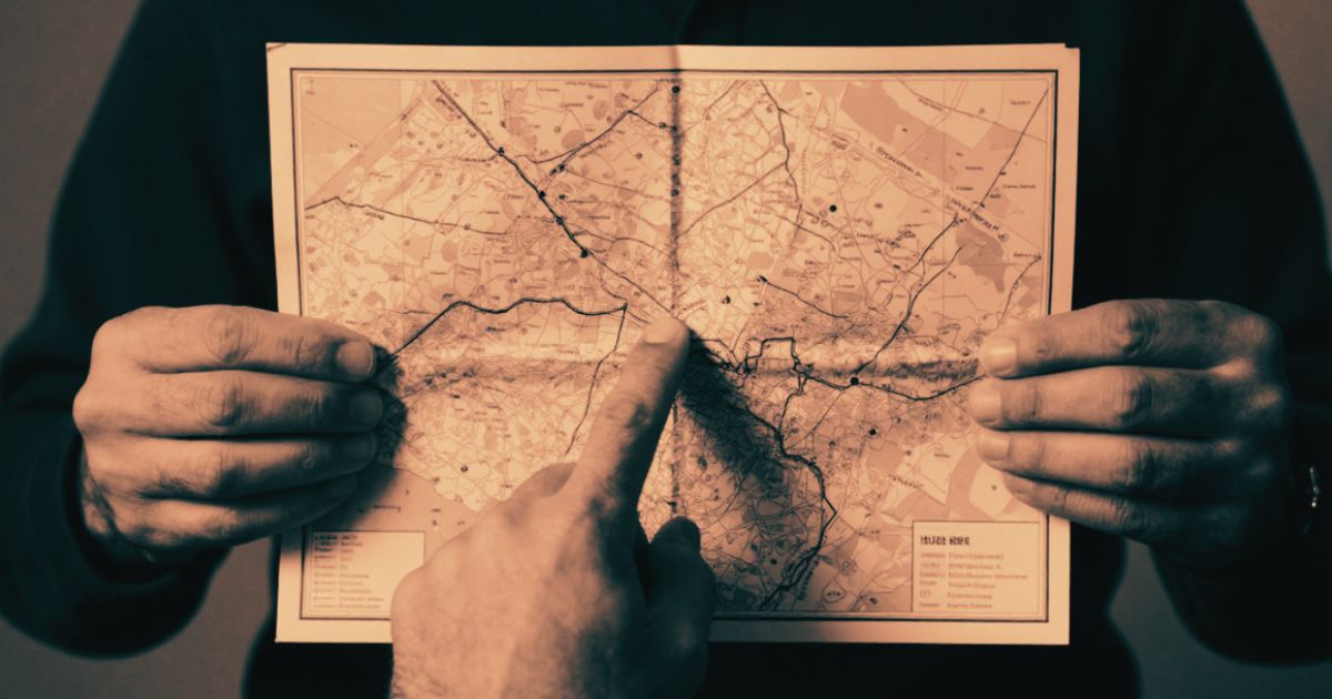 Two hands holding a folded map, one finger pointing to a precise location, strong directional light from one side