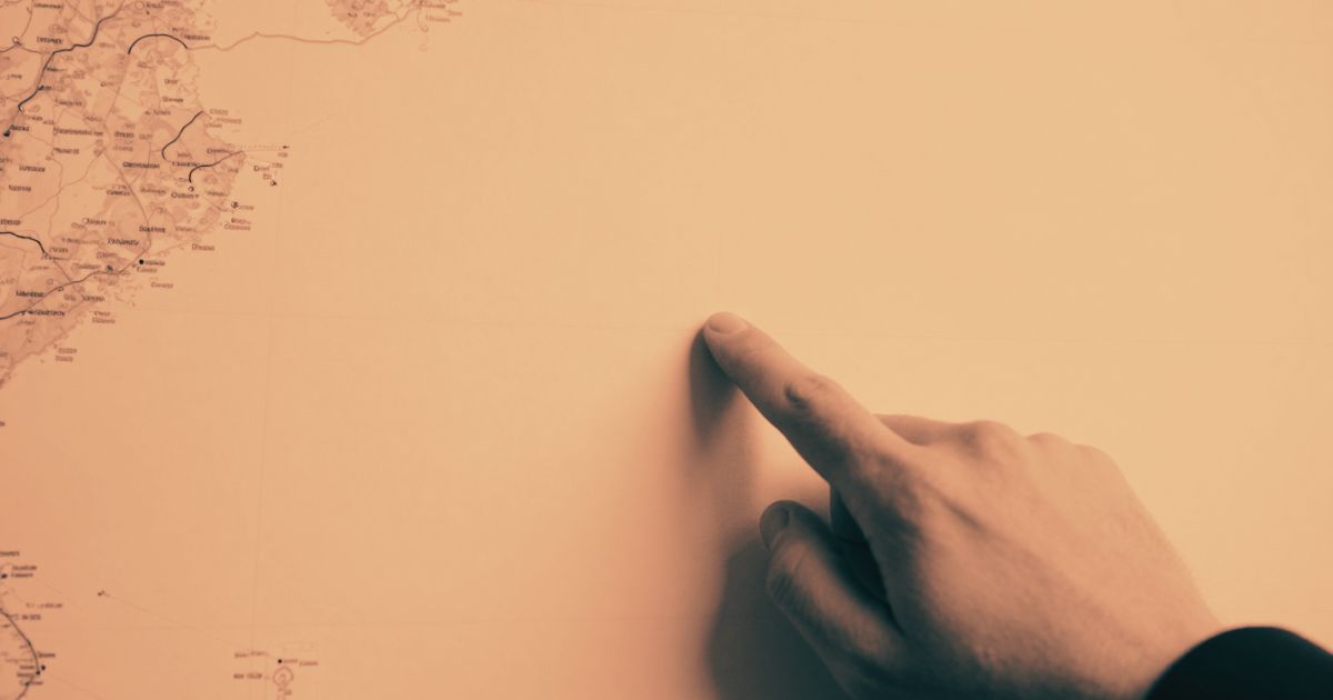 A single finger pointing at one precise point on a large blank map, close crop