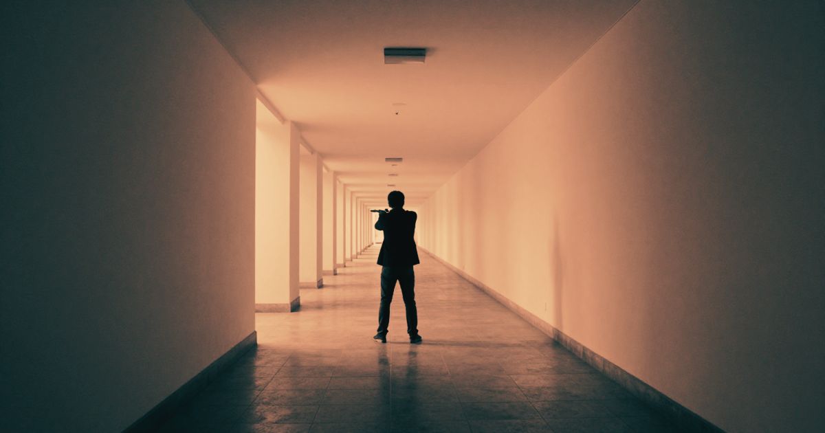 A figure standing at the end of a long empty corridor, small against the scale of the space